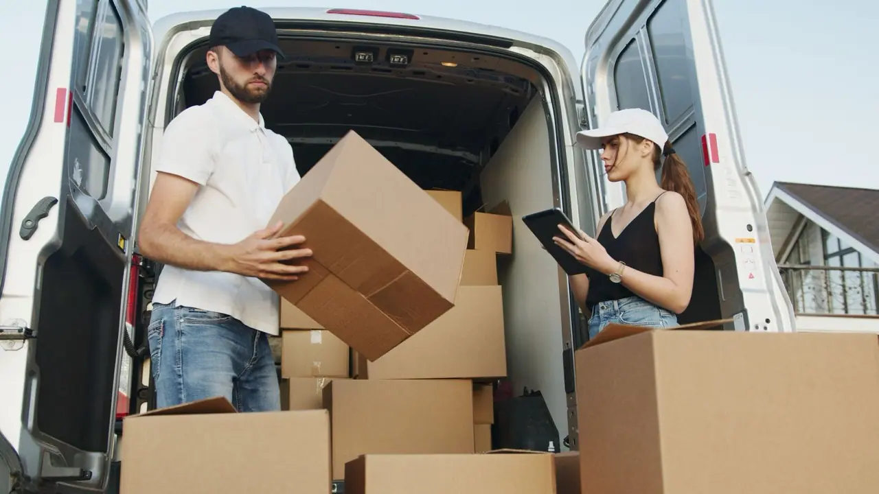 Two people loading moving boxes into the back of a van